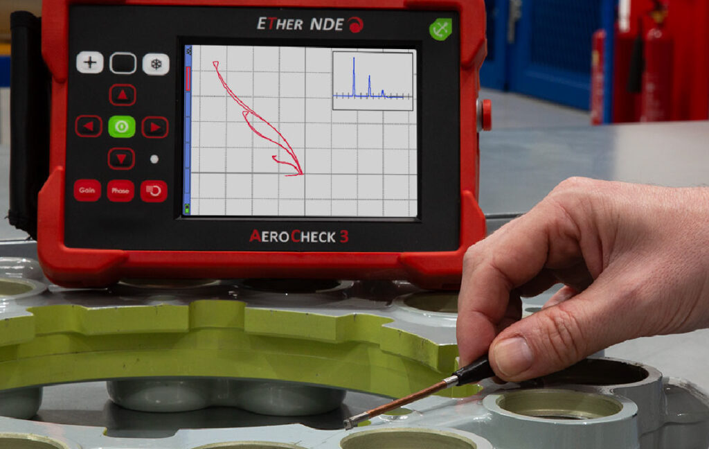 AeroCheck 3 eddy current flaw detector in use with a pencil probe on a metal testing surface
